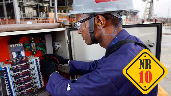 Eletricista uniformizado trabalhando em um painel elétrico externo, utilizando EPIs completos: capacete de segurança cinza, óculos de proteção transparentes, protetor auricular e luvas pretas. No canto inferior direito, há um selo amarelo de destaque com a inscrição 'NR 10'.