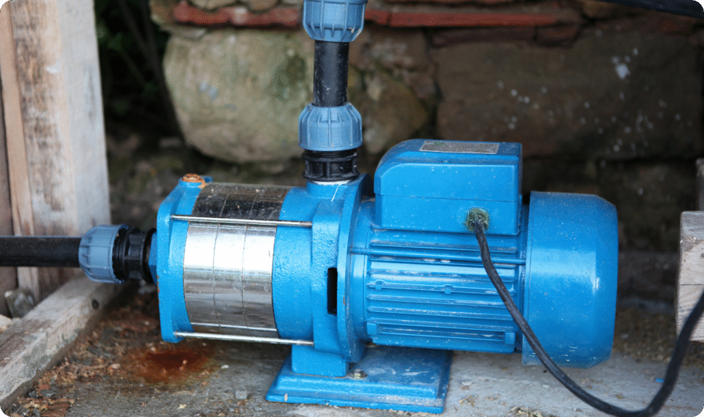 Bomba d'água centrífuga de cor azul instalada em base de concreto, conectada a tubulações de PVC, ilustrando um sistema de bombeamento residencial disponível na B.A Elétrica.